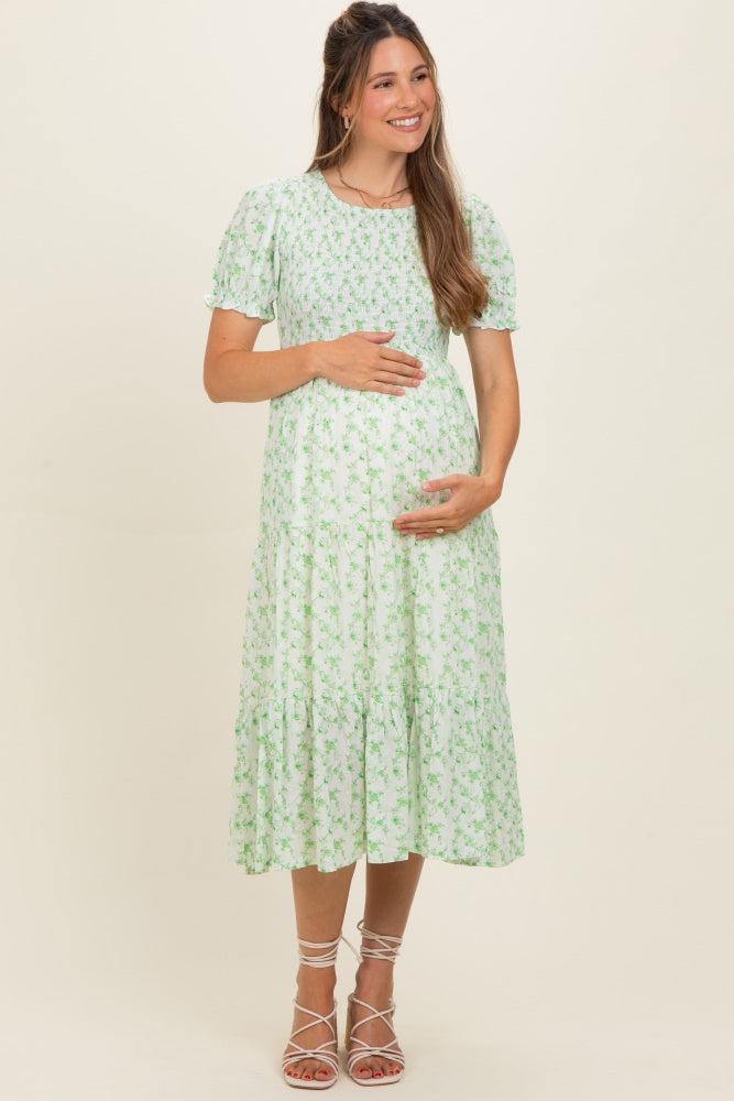 woman wearing a green floral maternity dress with short puff sleeves and holding her baby bump