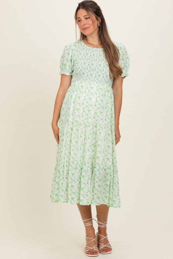 woman wearing a green floral maternity dress with short puff sleeves and a tiered skirt, showcasing her baby bump