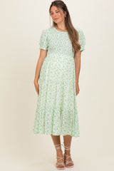 woman wearing a green floral maternity dress with short puff sleeves and a tiered skirt, showcasing her baby bump