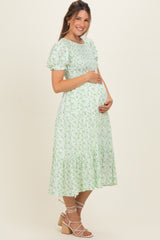 woman wearing a green floral maternity dress with short puff sleeves and holding her baby bump