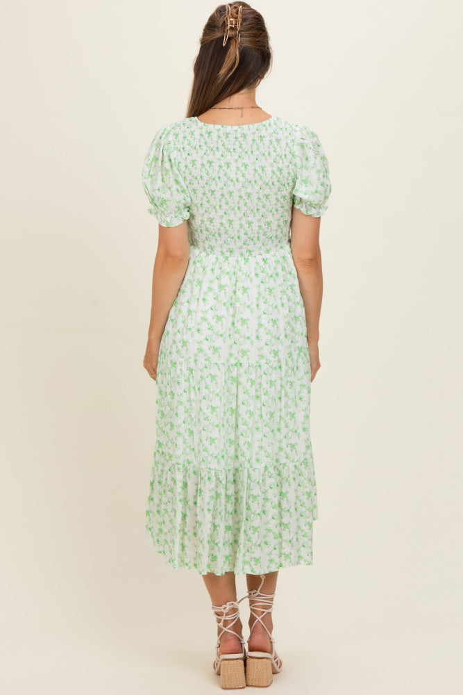 woman wearing a green floral maternity dress with puff sleeves and a tiered skirt, showing her baby bump from the back