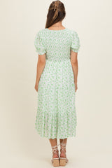 woman wearing a green floral maternity dress with puff sleeves and a tiered skirt, showing her baby bump from the back