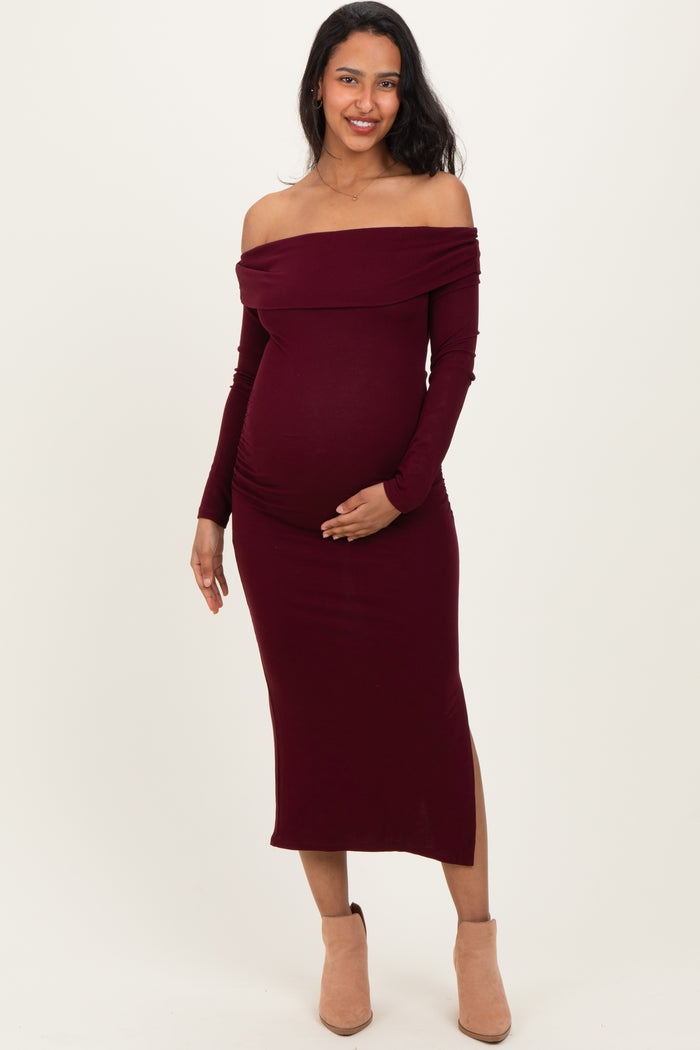 woman wearing a burgundy off-the-shoulder maternity dress and holding her baby bump