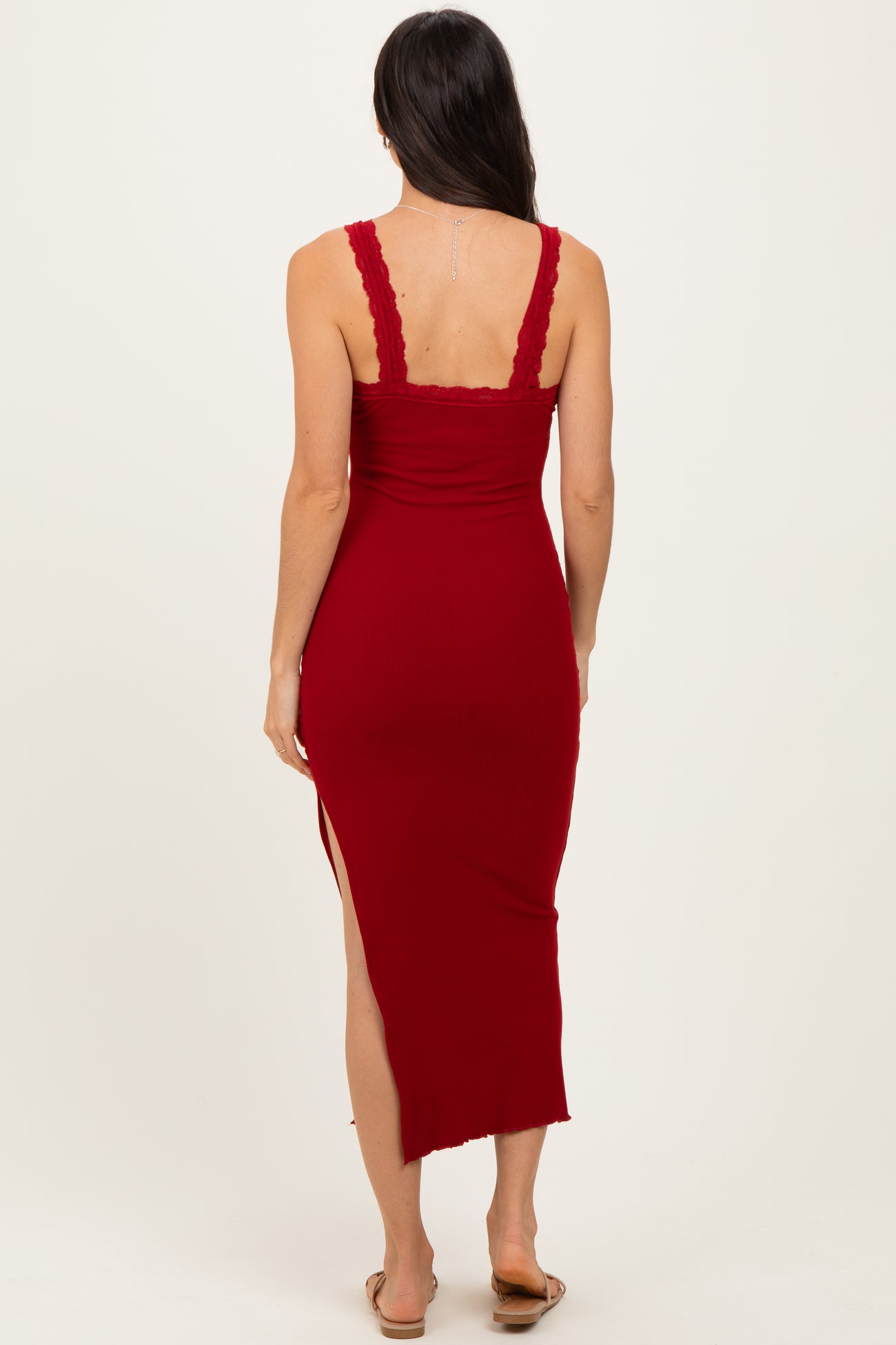 woman wearing a red ribbed midi dress with lace trim and a side slit, shown from the back