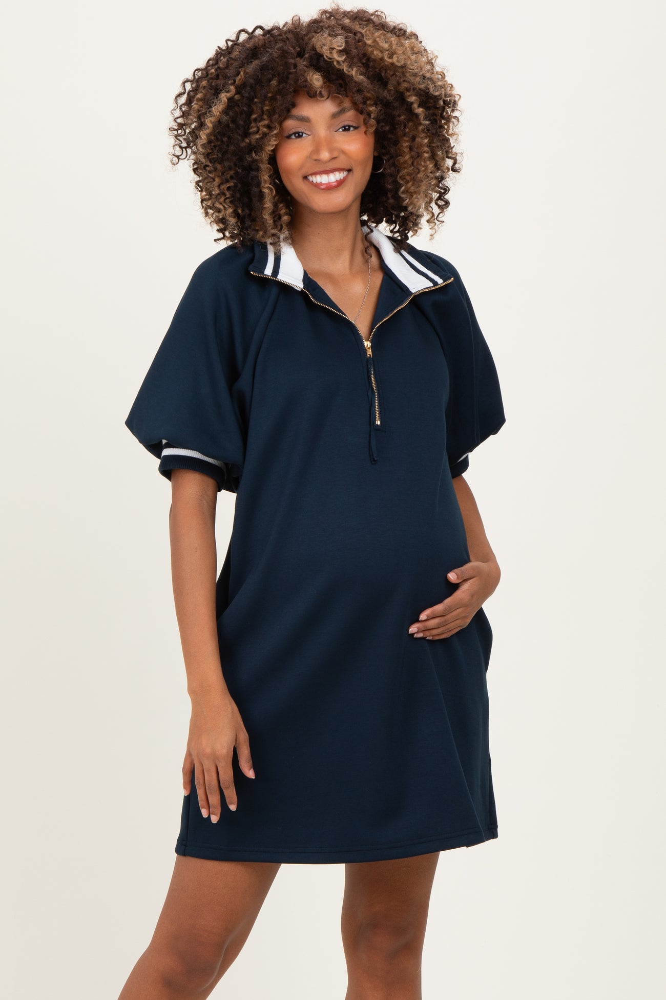 woman wearing a navy blue maternity dress with a half zipper and short sleeves, holding her baby bump