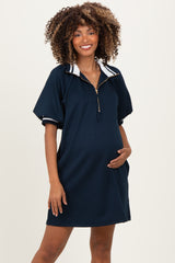 woman wearing a navy blue maternity dress with a half zipper and short sleeves, holding her baby bump