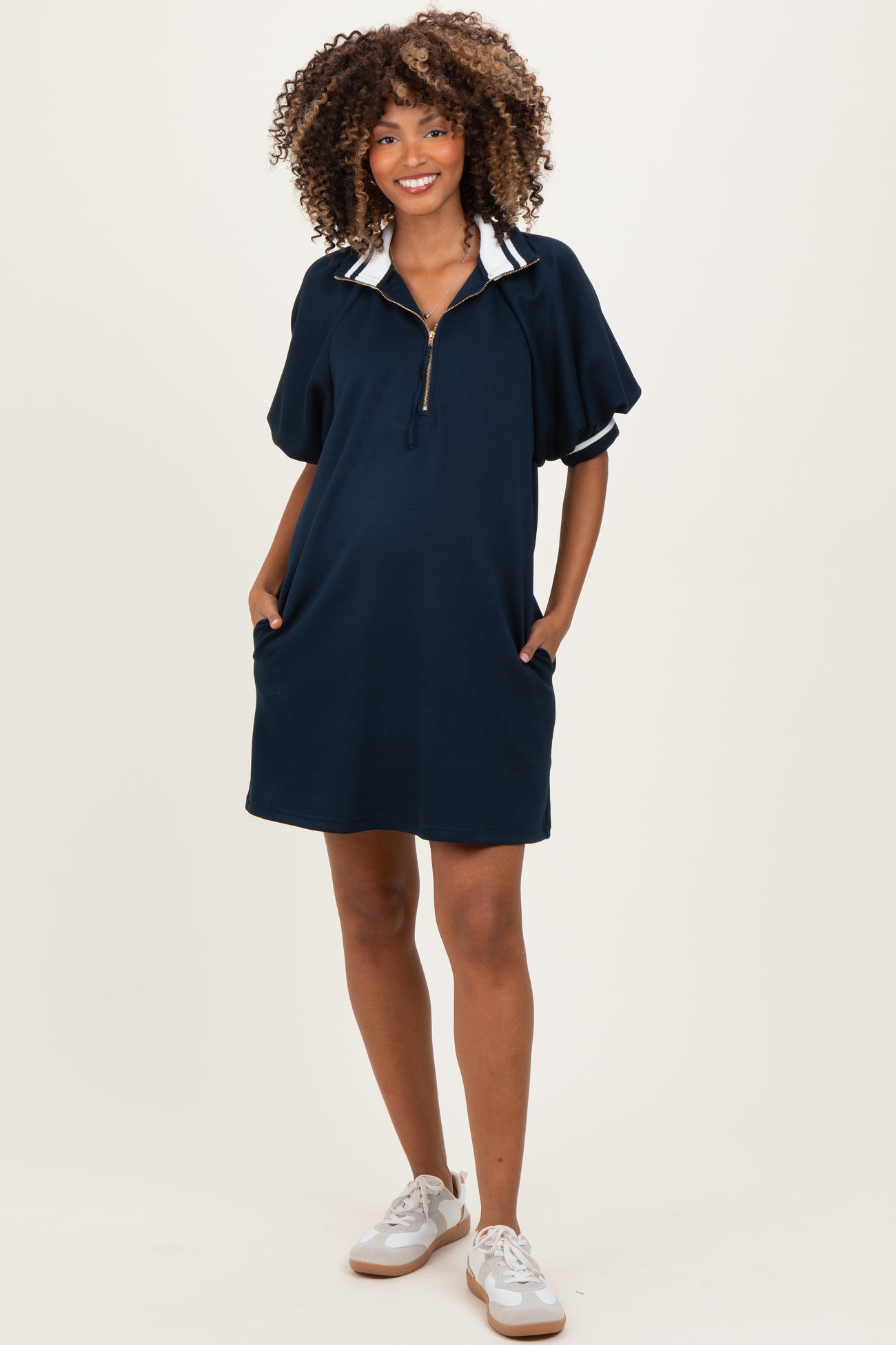 woman wearing a navy blue maternity polo dress with a zippered collar and side pockets