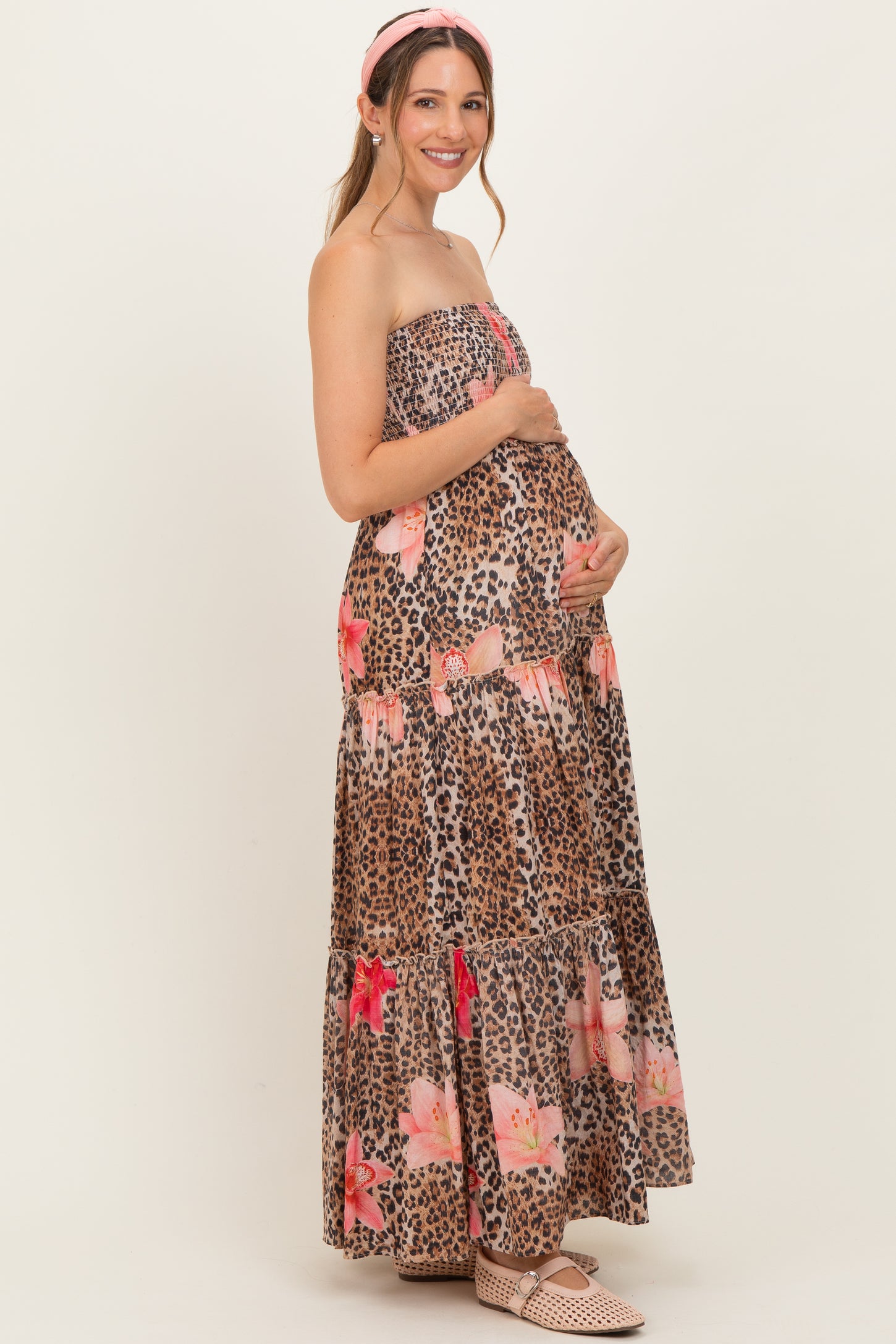 woman wearing a strapless leopard print maxi dress with floral details and holding her baby bump