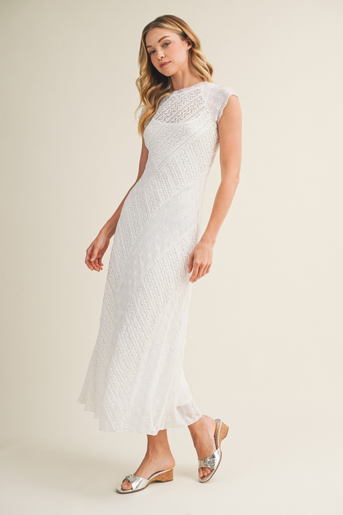 woman wearing a white sleeveless maxi dress with textured fabric and a scoop neckline, paired with silver sandals