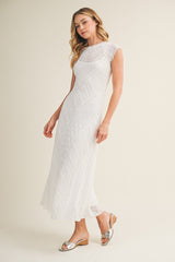 woman wearing a white sleeveless maxi dress with textured fabric and a scoop neckline, paired with silver sandals
