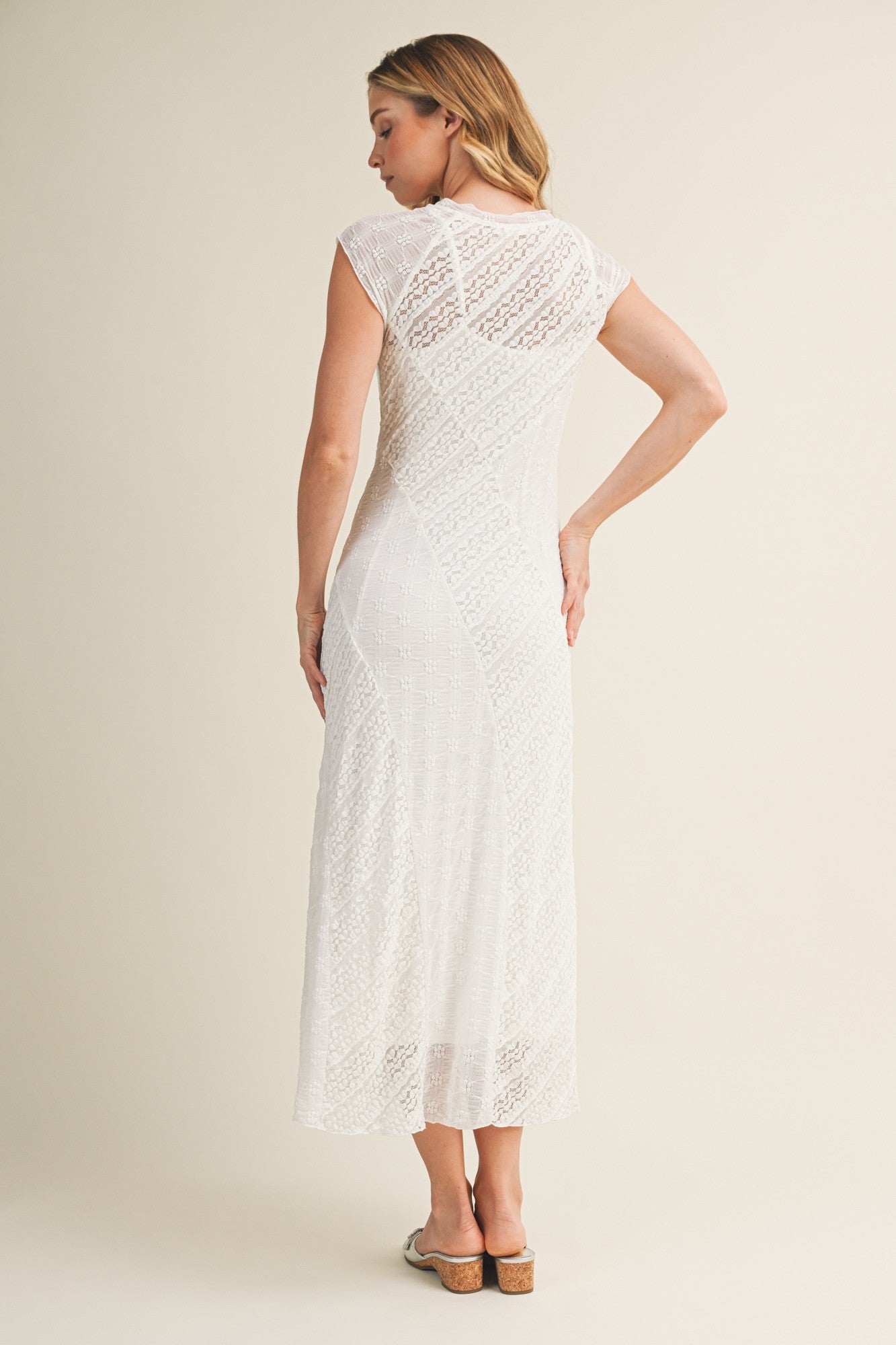 woman wearing a white knitted midi dress with cap sleeves, showing the back view and a fitted silhouette
