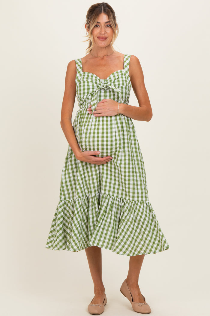 woman wearing a green and white gingham maternity dress with a ruffled hem and holding her baby bump