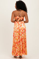 woman wearing a backless floral maxi dress with a tied detail and pleated skirt in shades of orange and pink