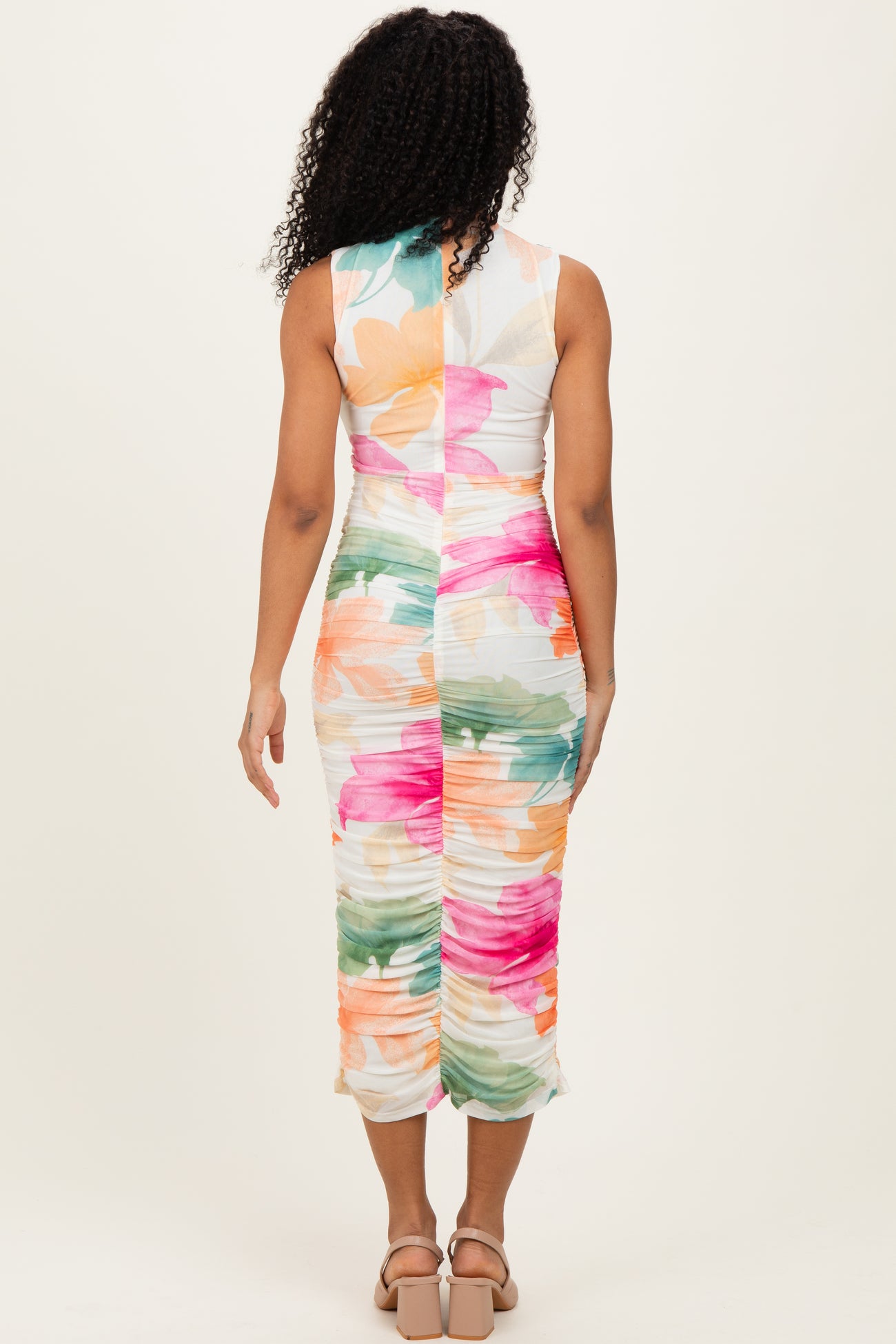 woman wearing a colorful floral print bodycon midi dress with a ruched back and sleeveless design