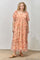 woman wearing a peach floral maxi dress with puff sleeves and a tiered hem, standing indoors on a concrete floor