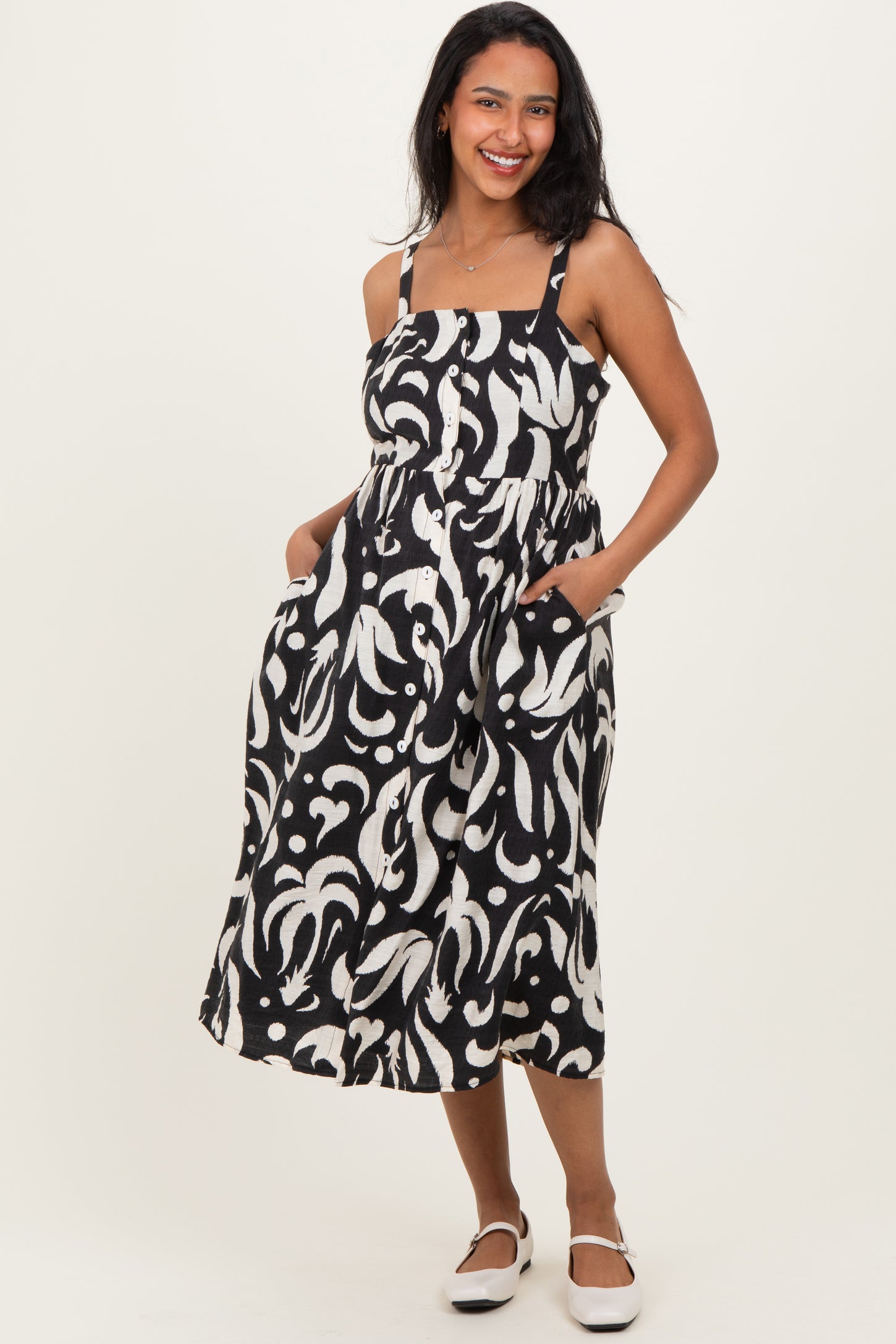 woman wearing a black and white patterned maternity dress with pockets and spaghetti straps, smiling at the camera