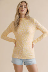 woman wearing a yellow long sleeve top with floral print and a scalloped neckline, paired with denim shorts