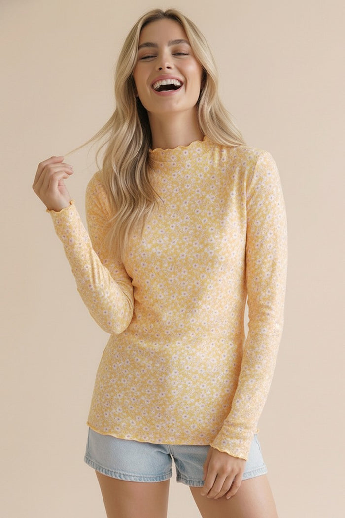 woman wearing a yellow long sleeve top with a floral pattern and a scalloped neckline, smiling against a beige background