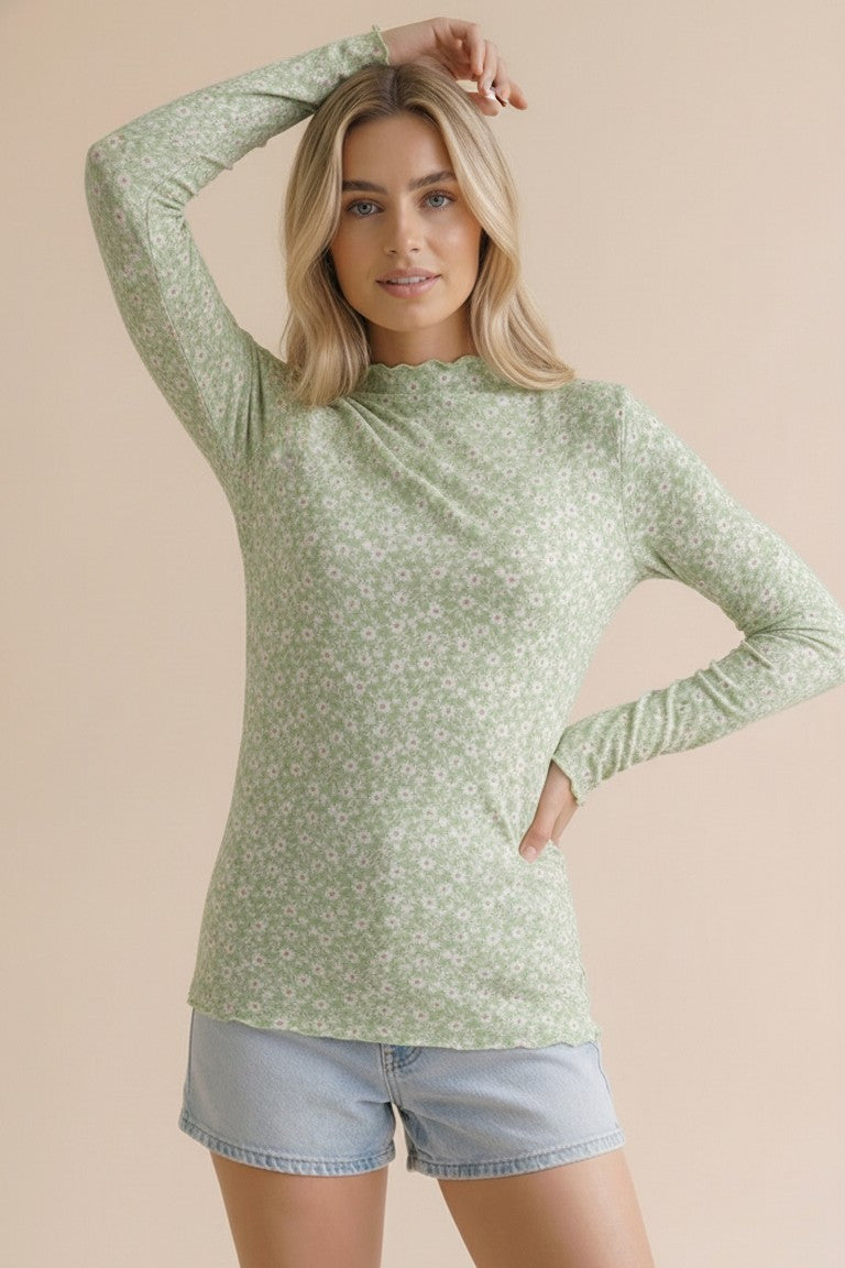 woman wearing a green long sleeve top with a floral pattern and light blue denim shorts