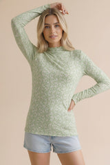 woman wearing a green long sleeve top with a floral pattern and light blue denim shorts