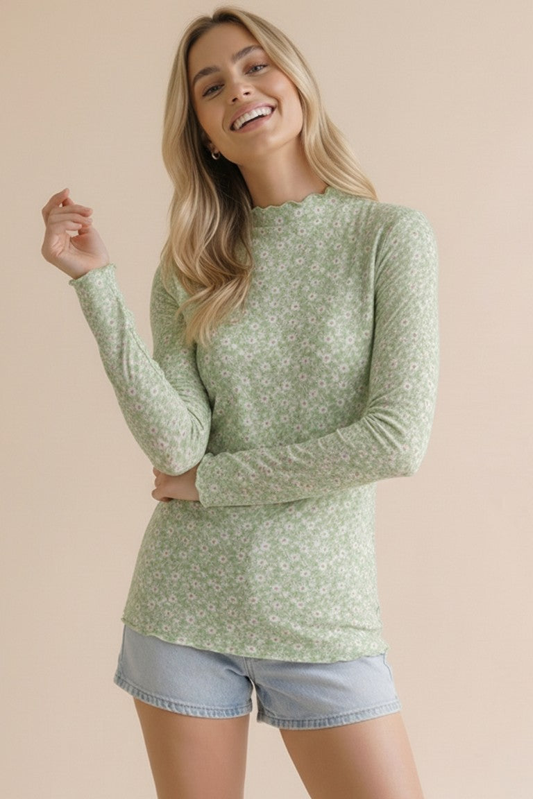 woman wearing a green long sleeve floral top with a scalloped neckline and light blue denim shorts