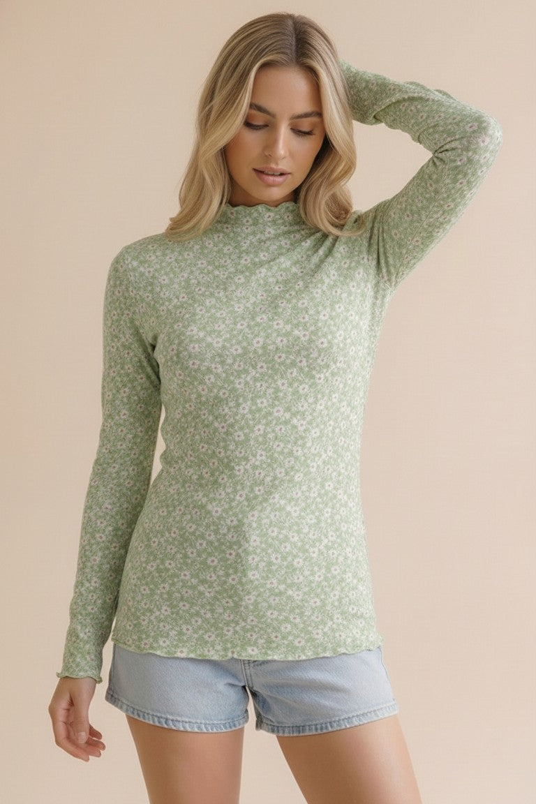 woman wearing a green long sleeve mock neck top with a floral pattern and distressed denim shorts
