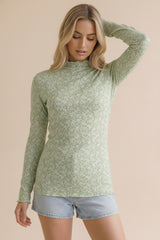 woman wearing a green long sleeve mock neck top with a floral pattern and distressed denim shorts
