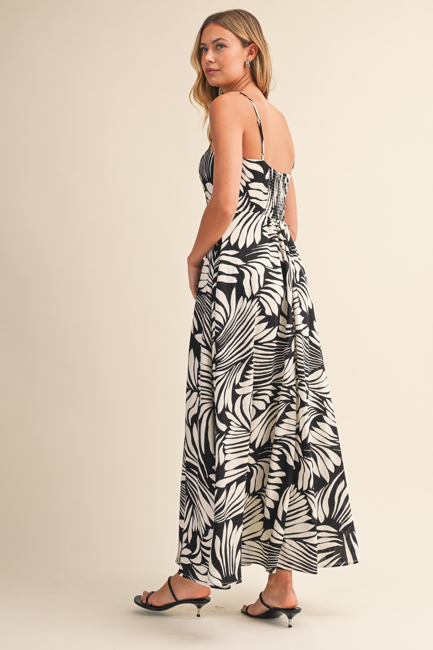 woman wearing a black and white tropical leaf print spaghetti strap maxi dress, standing with her back to the camera