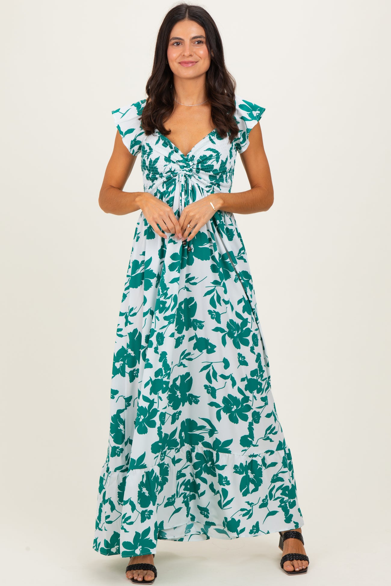 woman wearing a long floral maxi dress with cap sleeves and a cinched waist in shades of teal and white
