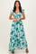 woman wearing a long floral maxi dress with cap sleeves and a cinched waist in shades of teal and white