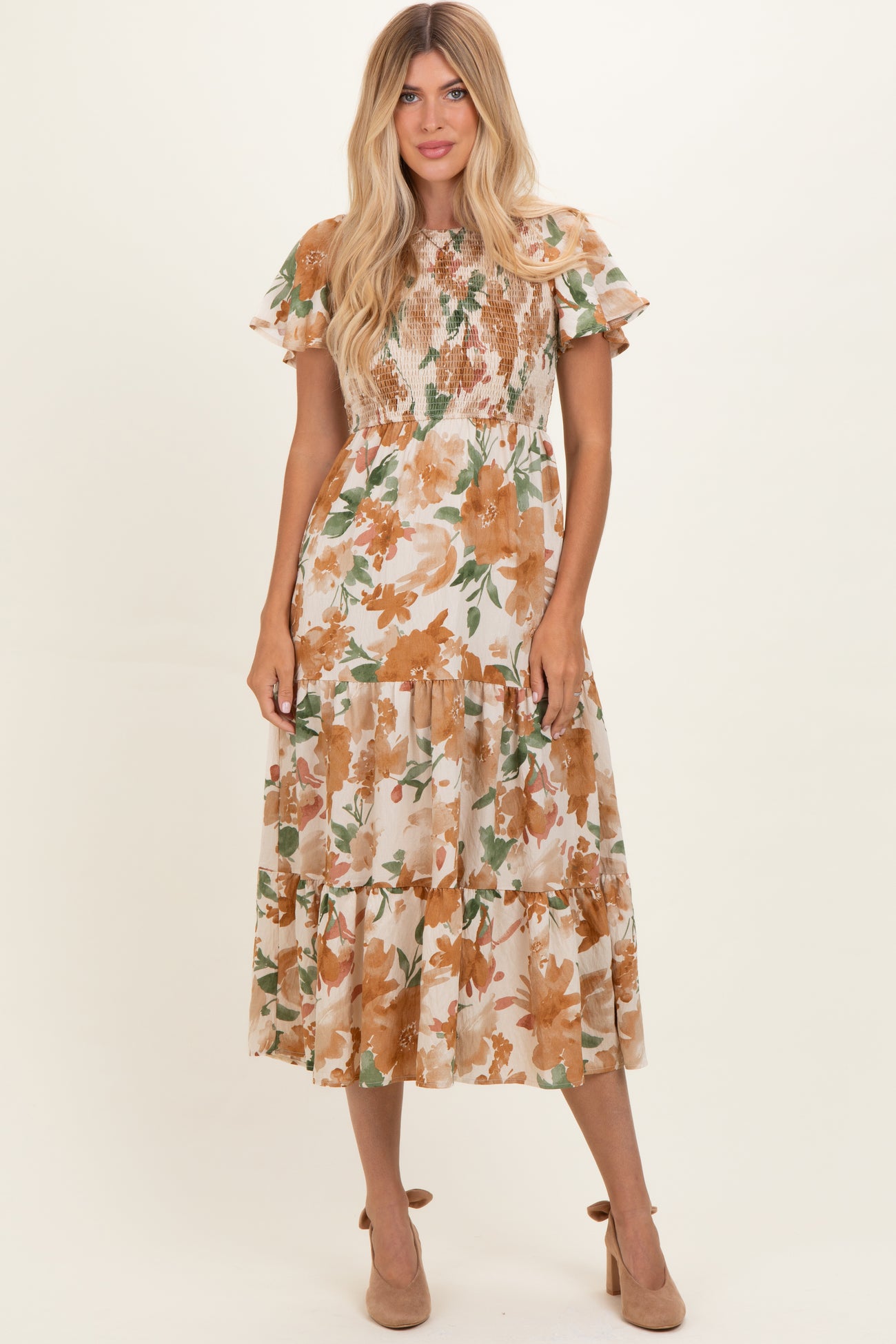 woman wearing a floral midi dress with ruffled sleeves and smocked bodice in shades of beige, orange, and green