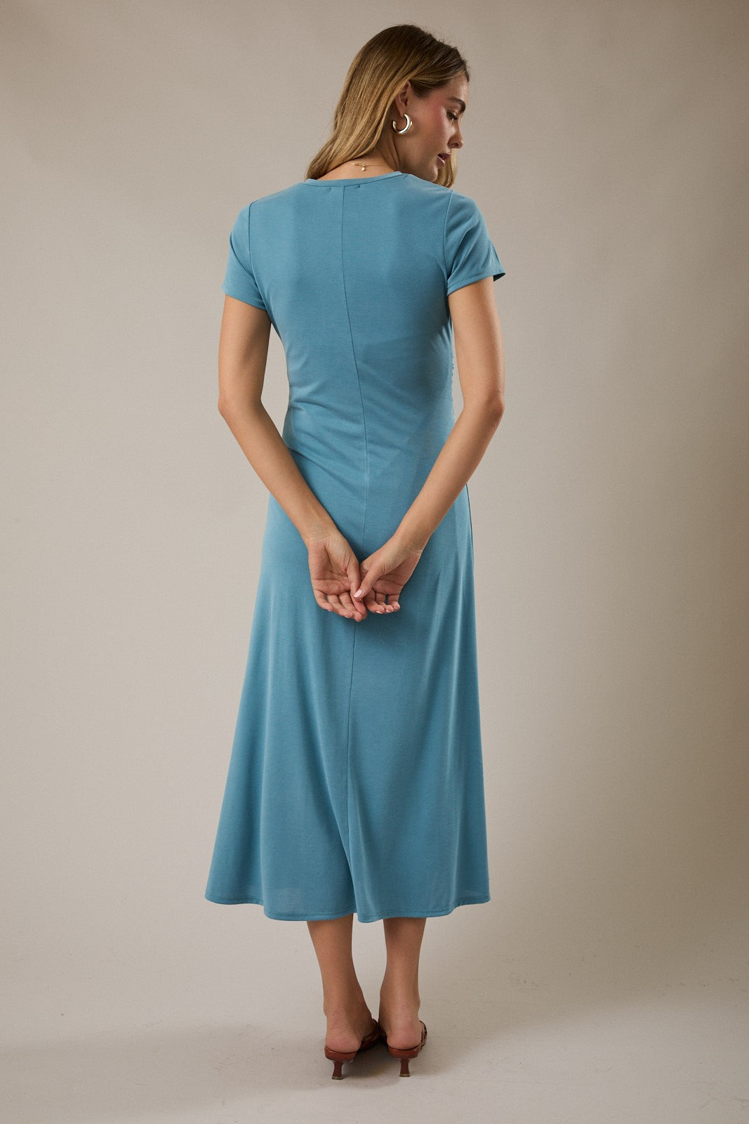 woman wearing a short sleeve blue midi dress, facing away with her hands behind her back