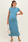 woman wearing a turquoise maternity maxi dress with short sleeves and holding a crocheted bag, showing her baby bump