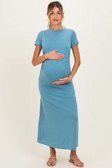 woman wearing a teal maternity maxi dress and gently cradling her baby bump