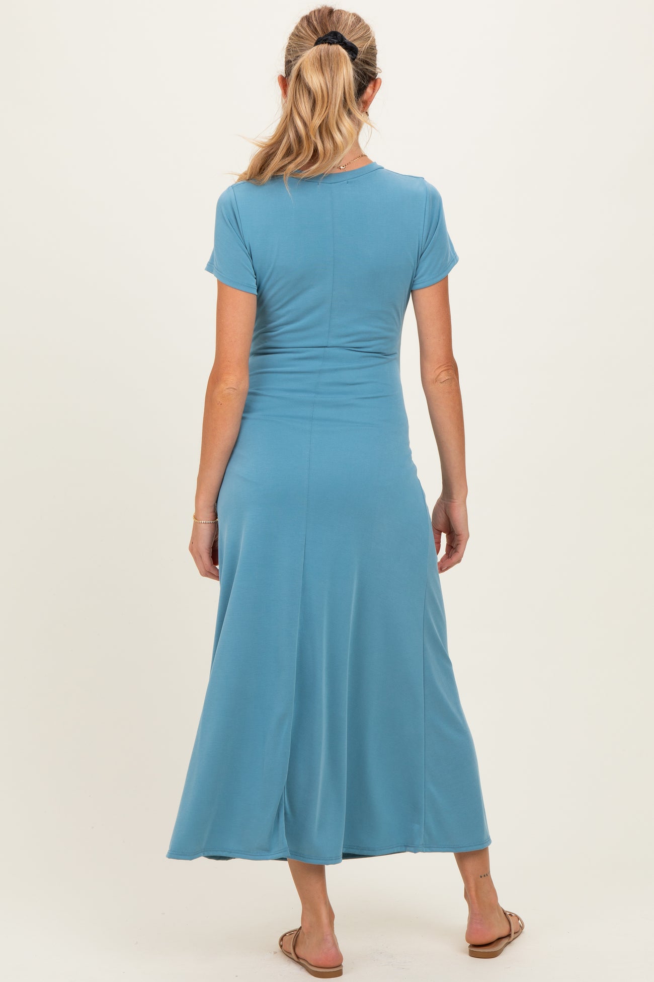 woman wearing a teal short sleeve maternity dress, showing a flowing skirt from the back, casual style