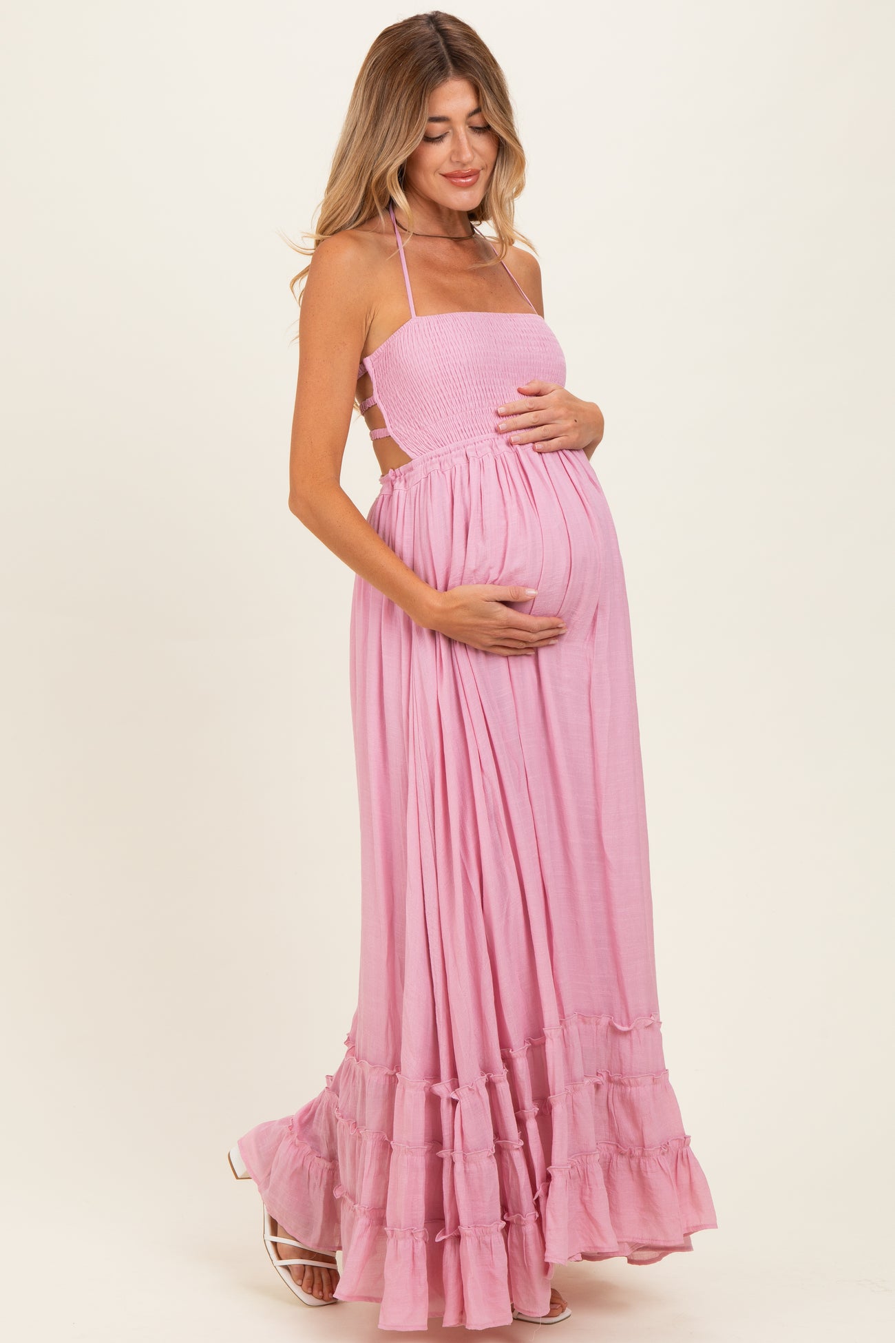 woman wearing a light pink maternity maxi dress with a smocked bodice and ruffled hem, gently cradling her baby bump