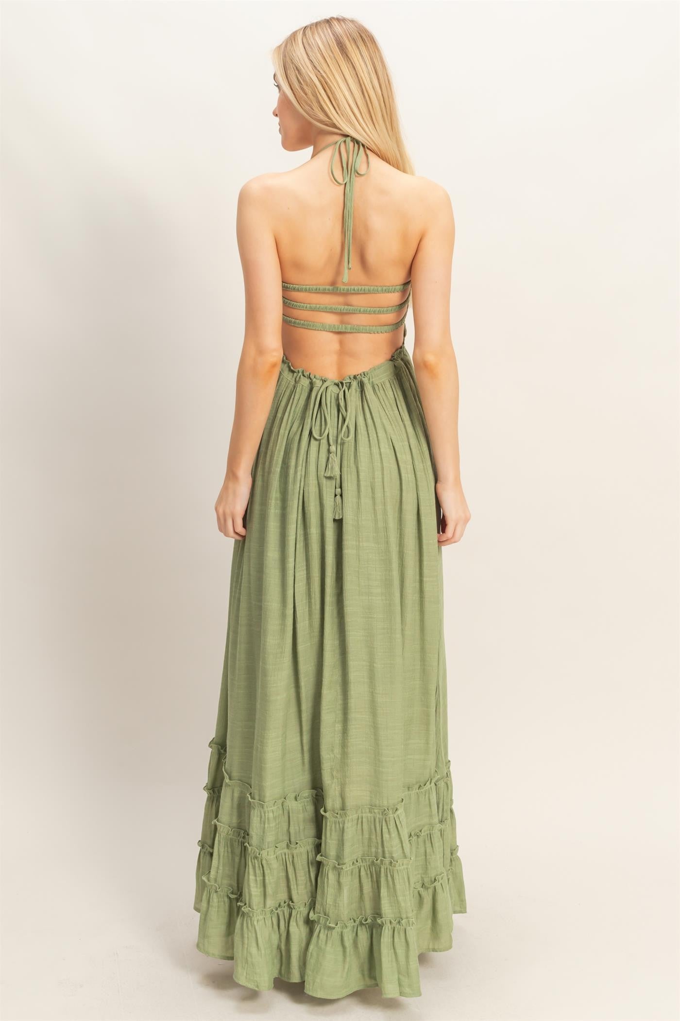 woman wearing a green maxi dress with a halter neck and ruffled hem, showing an open back design