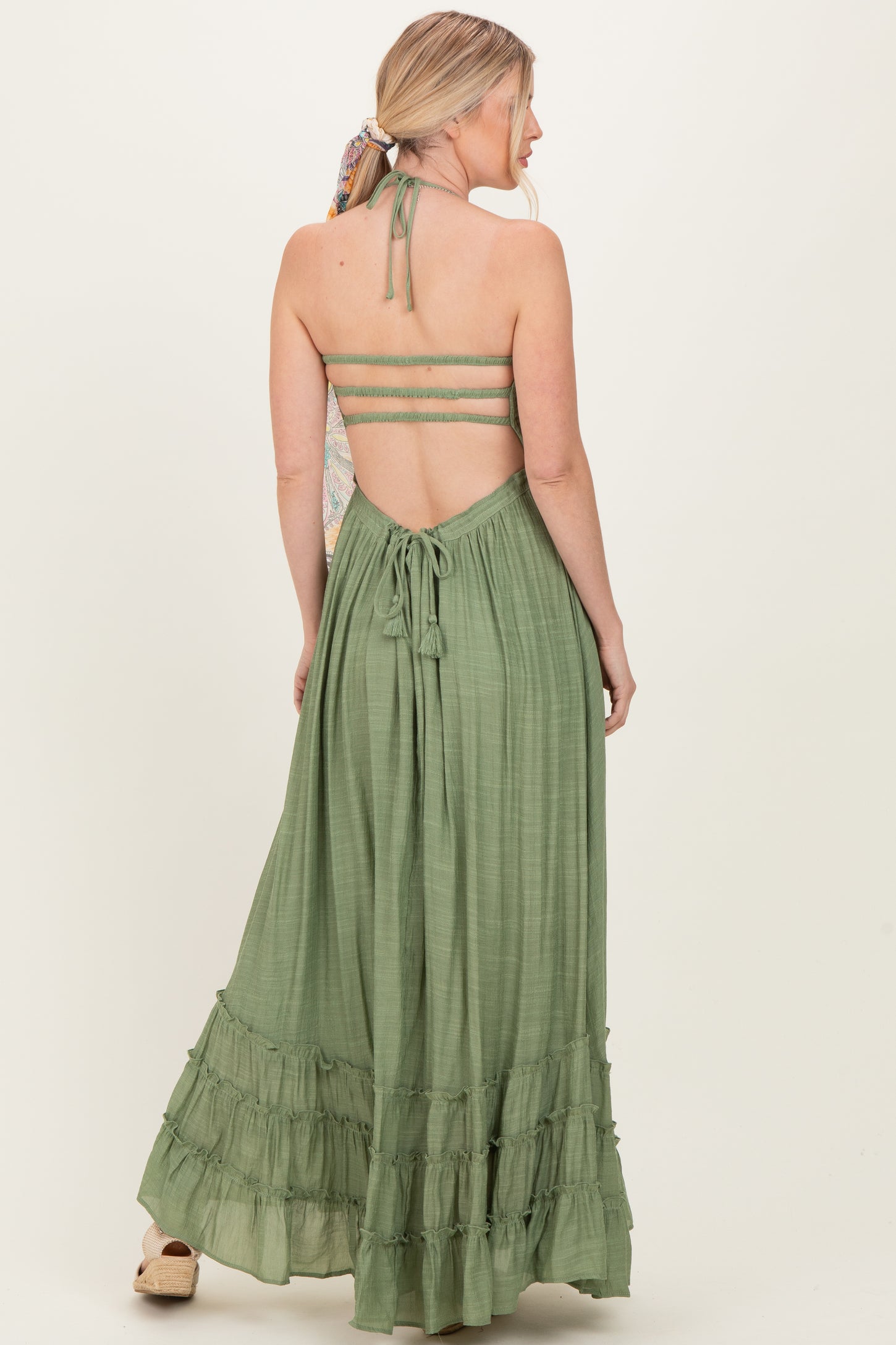 woman wearing an olive green maxi dress with a tie-back and ruffled hem, featuring a halter neckline and open back