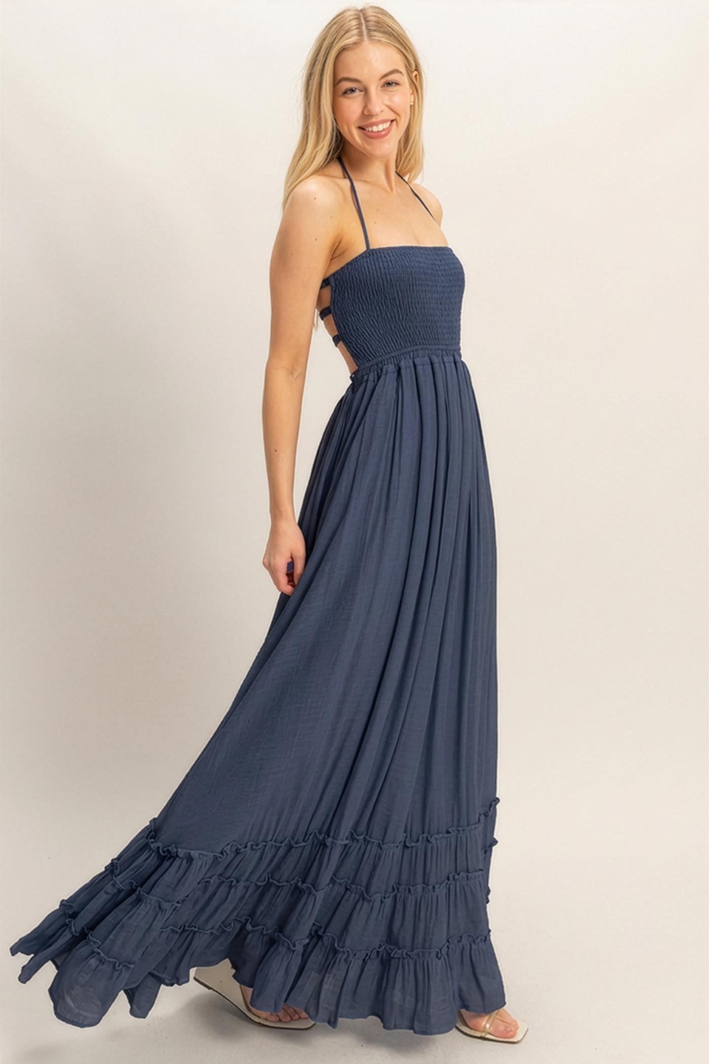 woman wearing a navy blue maxi dress with a smocked bodice and ruffled hem, smiling and posing against a light background