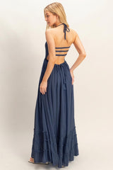 woman wearing a navy blue maxi dress with adjustable straps and tiered ruffle details at the hem, showing the back view