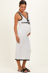 woman wearing a white maternity dress with black trim and a bow detail, showcasing her baby bump
