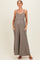 woman wearing a taupe maternity jumpsuit with pockets and adjustable straps, showcasing her baby bump