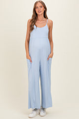 woman wearing a light blue maternity jumpsuit with spaghetti straps and side pockets, showcasing her baby bump
