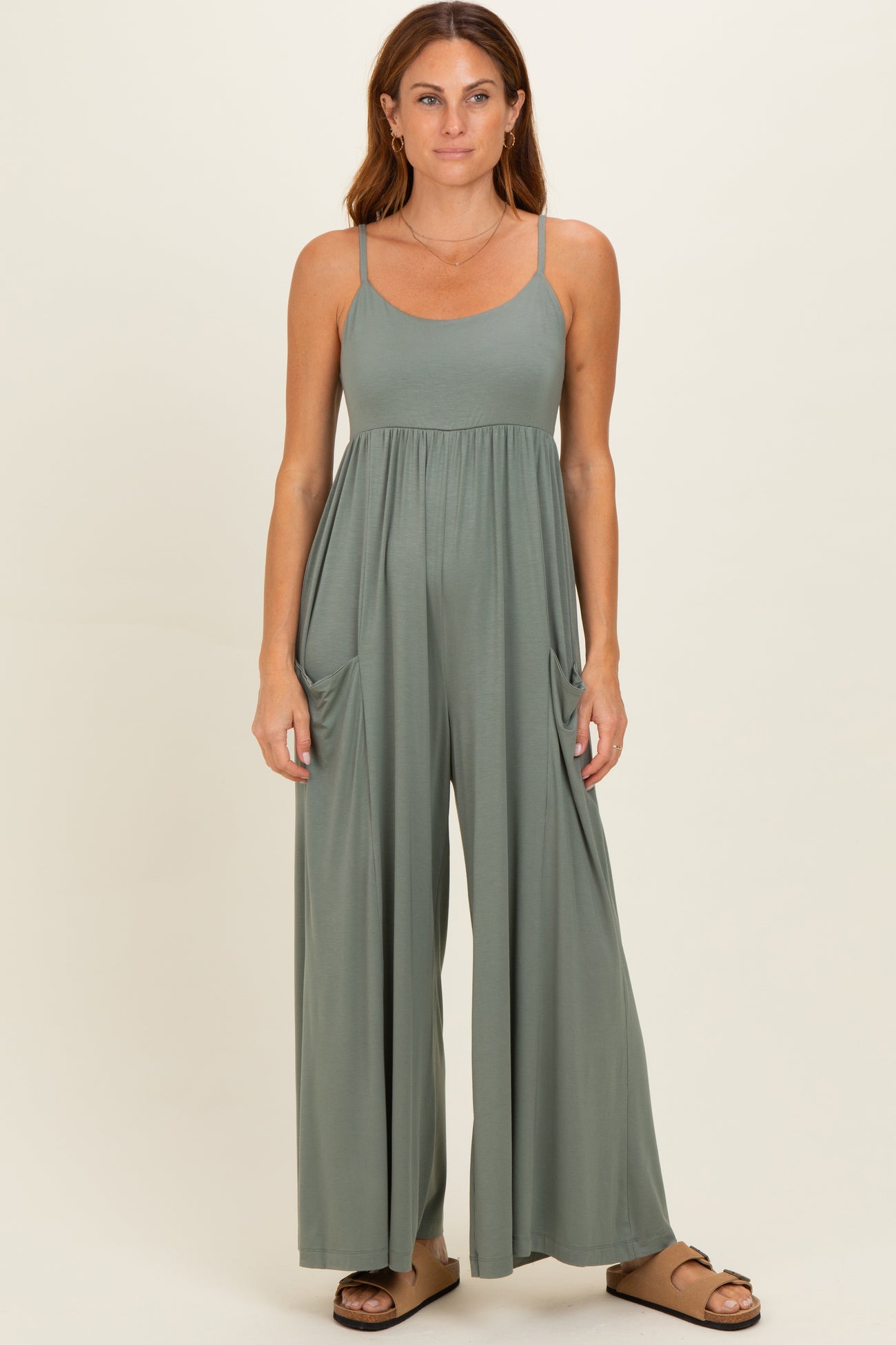 woman wearing a sage green sleeveless jumpsuit with wide legs and side pockets
