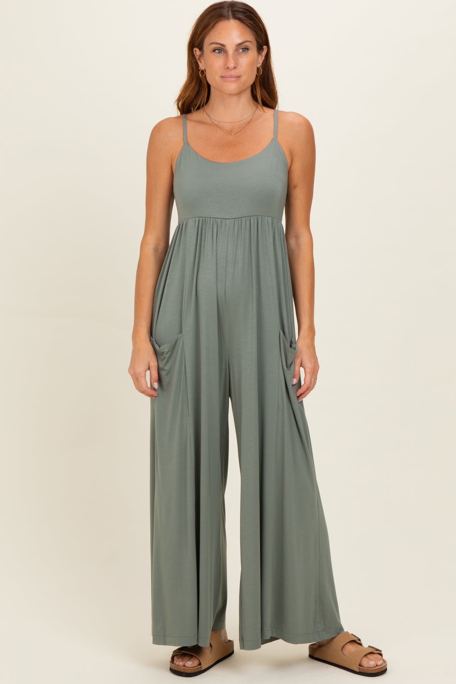 woman wearing a sage green sleeveless jumpsuit with wide legs and side pockets