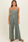 woman wearing a sage green sleeveless jumpsuit with wide legs and side pockets