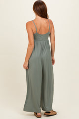 woman wearing a back view of a sage green sleeveless wide-leg jumpsuit with adjustable straps