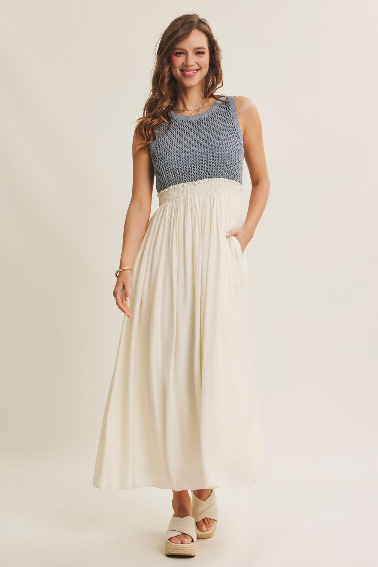 woman wearing a striped blue and white maxi dress with a fitted bodice and a flowy white skirt, standing with hands in pockets
