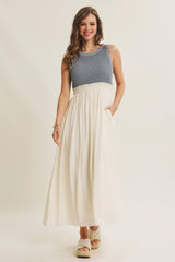 woman wearing a striped blue and white maxi dress with a fitted bodice and a flowy white skirt, standing with hands in pockets