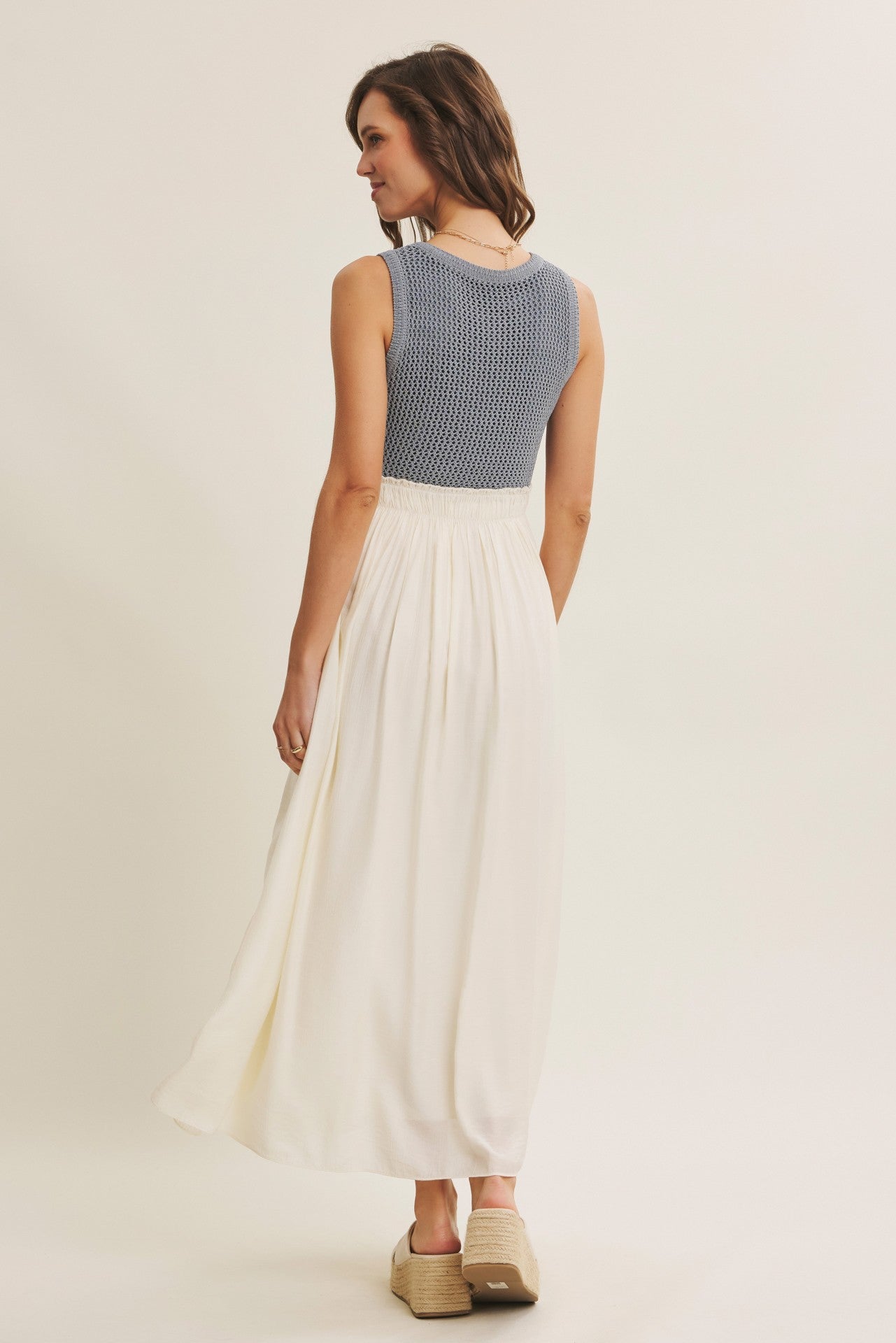 woman wearing a sleeveless blue knit top with a white maxi skirt and standing with her back to the camera